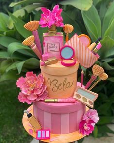 there is a pink cake with makeup on top and flowers in the middle that says bela