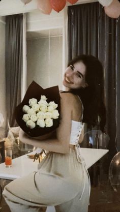 a woman holding a bouquet of flowers in front of a table with balloons hanging from the ceiling