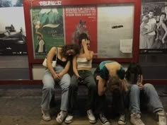 four people sitting on a bench in front of posters and signs at a subway station