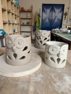 three white vases sitting on top of a wooden table in a room filled with shelves