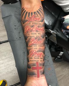 a person with a tattoo on their arm holding up a cross and bible verses