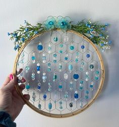 a person is holding up a circular beaded wall hanging with blue beads and flowers on it