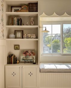 a white book shelf with books and other items on it in front of a window