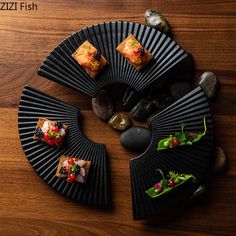 four small pieces of sushi are arranged on a black plate, surrounded by rocks and seaweed