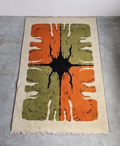 an orange, green and black rug on the floor with a white wall in the background