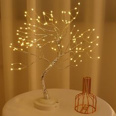 a lighted tree is sitting on a table next to a small vase with lights in it