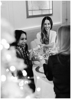 three women sitting at a table laughing and having dinner with candles on the table in front of them