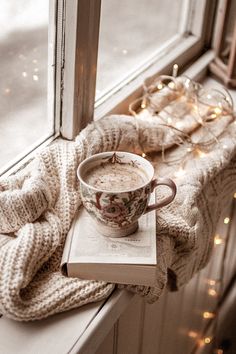 a cup of coffee sitting on top of a book next to a window sill