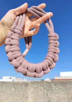 a hand holding a pink rope in the shape of a circle on top of a cement wall