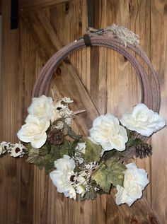 a wreath with white flowers hanging on a wooden wall next to a rope and wood door