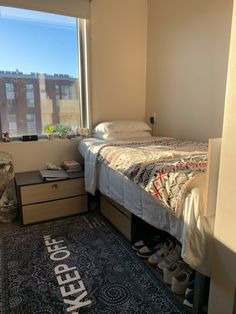 a bedroom with a bed, dresser and rug in front of a window that reads keep off