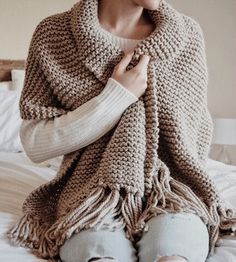 a woman sitting on top of a bed wearing a crocheted shawl