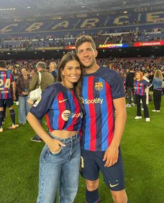 a man and woman posing for a photo in front of a crowd at a soccer game