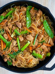 stir fried noodles with chicken and vegetables in a skillet on a wooden table top