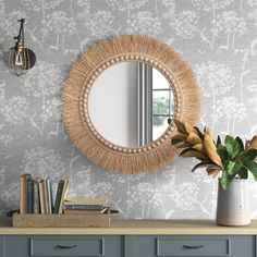 a mirror on the wall next to a dresser and vase with flowers in it,