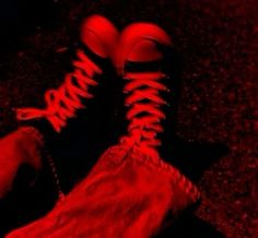 a person's feet with red laces on them and their shoes in the dark