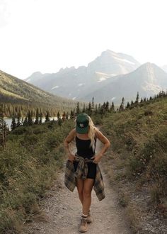 a woman walking down a dirt road in the mountains with her hands on her hips