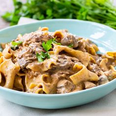 a blue bowl filled with pasta covered in mushroom sauce and garnished with parsley