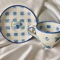 two cups and saucers are sitting on a white tablecloth with blue checkered designs