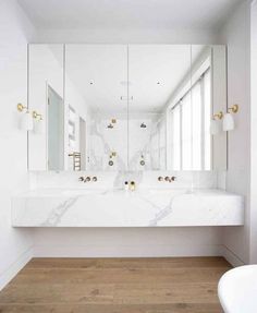 a white bathroom with marble counter tops and gold faucets on the mirror wall