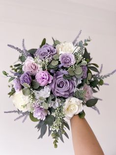 a person holding a bouquet of purple and white flowers with greenery on the stems