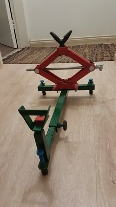 a red and green cart sitting on top of a hard wood floor next to a white wall