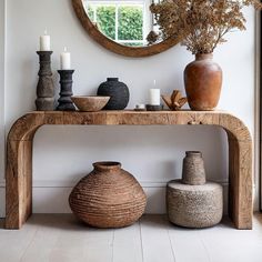 a wooden table with vases and candles on it in front of a round mirror