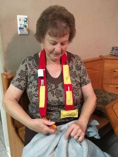 an older woman sitting on a chair with a scarf around her neck and holding something in her hands