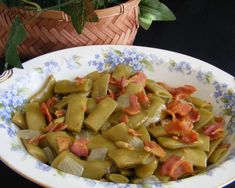 a bowl filled with green beans and bacon on top of a table next to a potted plant