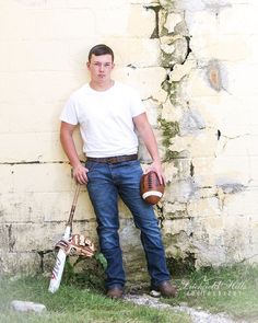 a man leaning against a wall holding a baseball bat and glove