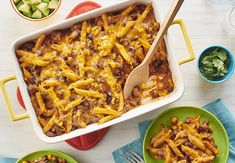 two green plates filled with chili and cheese covered casserole next to bowls of salad