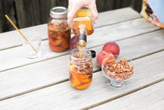 a person pouring syrup into jars filled with peaches and pecans on a picnic table