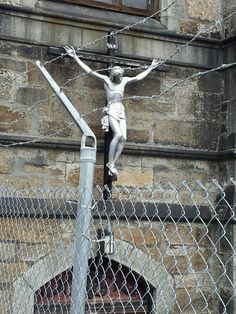 there is a statue on top of a pole in front of a building that has a chain link fence around it