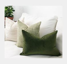 the pillows are green and white on the couch in front of a potted plant