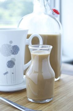 there are two cups and a pitcher on the table with spoons next to it