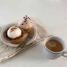 a cup of coffee next to a pastry on a napkin with a fork and spoon