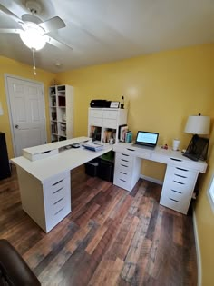 a room with yellow walls and wooden floors has a white desk, drawers, and laptop on it