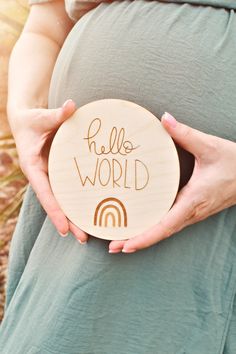 a pregnant woman holding a wooden plate with the words hello world written on it in front of her belly