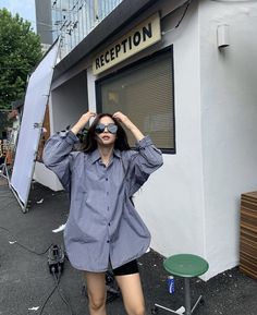 a woman standing in front of a building with her hands on her head while wearing sunglasses