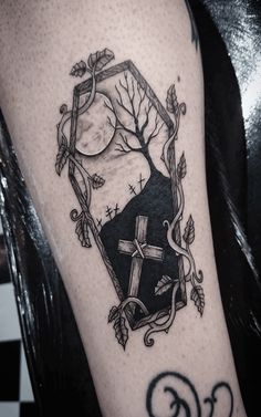 a black and white photo of a cross tattoo on the arm, with vines around it