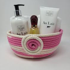 a pink and white rope basket with soap, lotion, hand sanitizer and other items in it