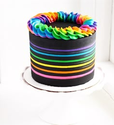 a multicolored cake sitting on top of a white table next to a window