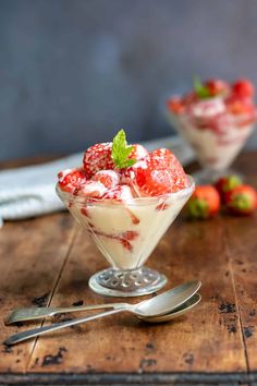 two dessert dishes with strawberries and whipped cream in them on a wooden table next to silverware