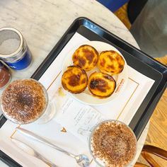 three desserts are on a tray with spoons and two cups next to each other