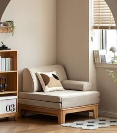 a living room scene with focus on the couch and book shelf in the corner near the window