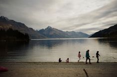 people walking on the shore of a lake with mountains in the background