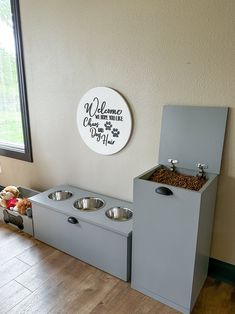 two dog bowls in front of a welcome sign with a teddy bear on the floor