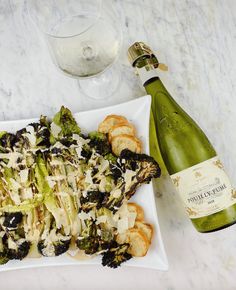 a white plate topped with broccoli and cheese next to a bottle of wine