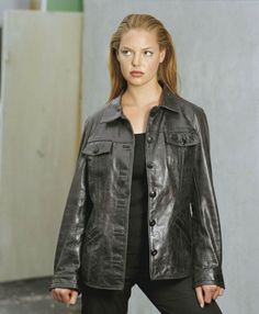 a woman wearing a black leather jacket and pants standing in front of a white wall