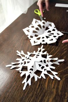 someone cutting out paper snowflakes on a table